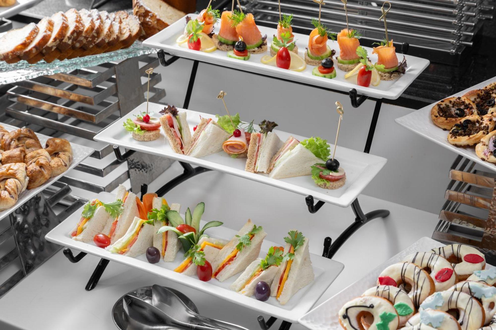 Al Aqeeq Madinah Hotel Медина Екстериор снимка The photo shows a tiered display of assorted appetizers and snacks arranged on white rectangular plates. 

1. **Top Tier**: Contains small bites featuring smoked salmon garnished with greenery, and some with colorful cherry tomatoes on toothpicks. 

