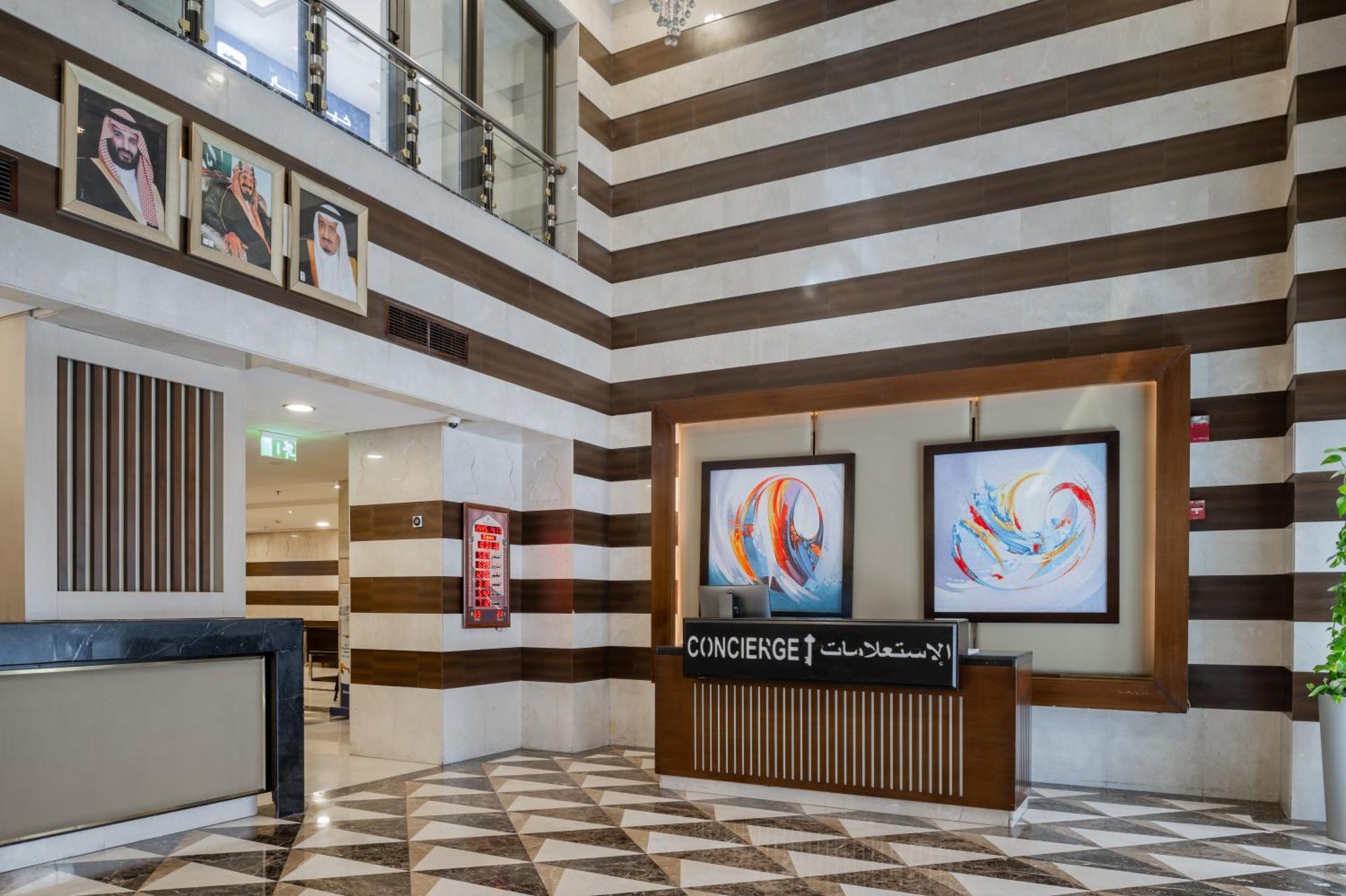 Al Aqeeq Madinah Hotel Медина Екстериор снимка The photo shows a modern hotel lobby area characterized by its stylish design. The walls feature a pattern of horizontal stripes in different shades, creating a sophisticated atmosphere. To the left, there is a reception area with a sleek desk labele