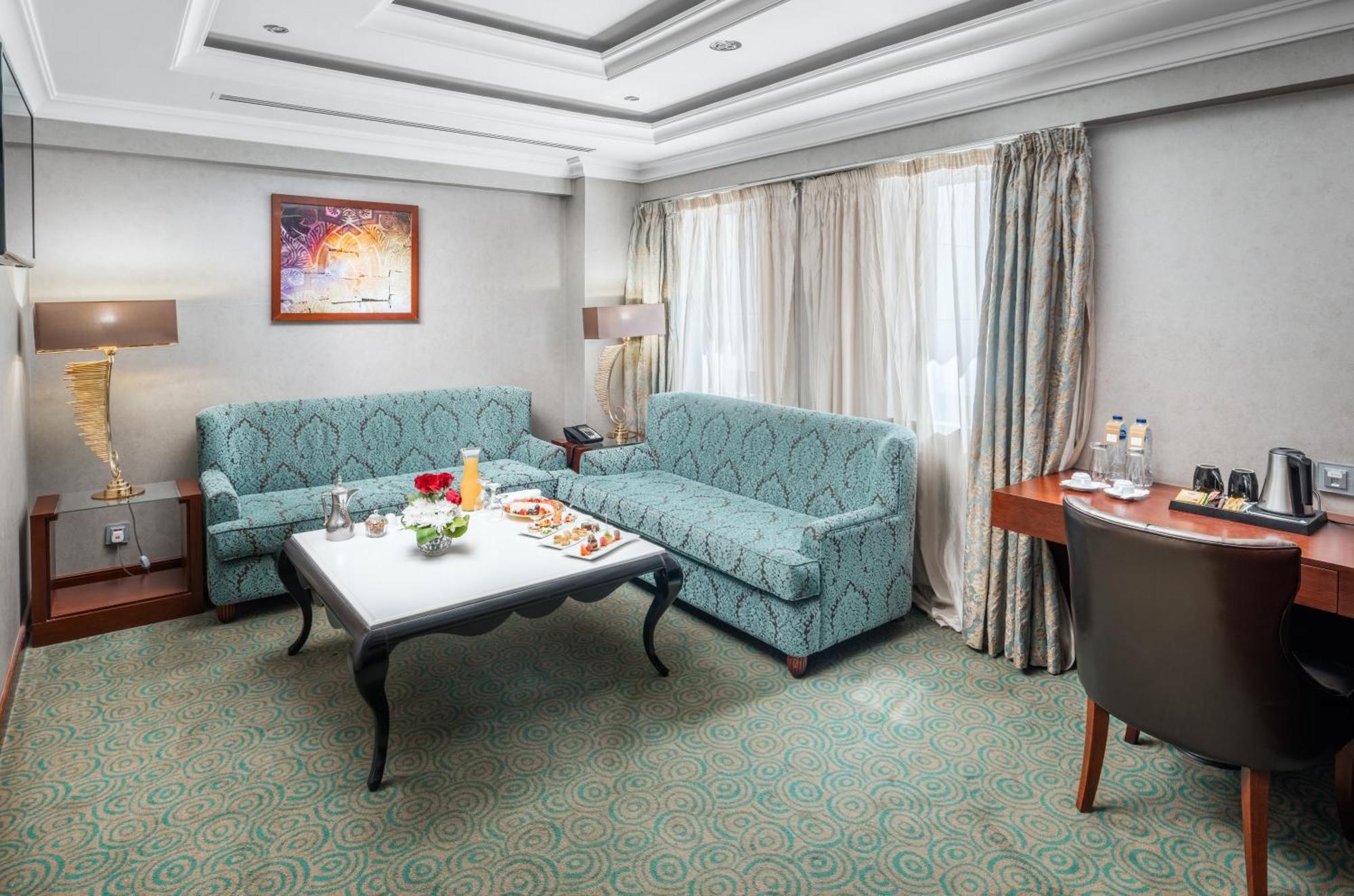 Al Aqeeq Madinah Hotel Медина Екстериор снимка The photo shows a cozy hotel room or lounge area. It features two light blue sofas arranged around a low coffee table. On the table, there are snacks or refreshments arranged aesthetically. The room has a neutral color palette with a textured carpet 