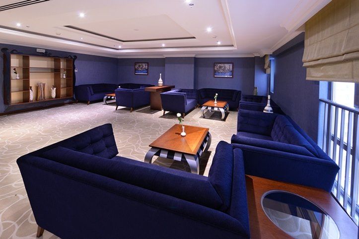 Al Aqeeq Madinah Hotel Медина Екстериор снимка The photo shows a modern lounge area featuring a sophisticated design. The room is painted in a deep blue color, creating a calm and elegant atmosphere. There are several dark blue sofas arranged around a central wooden coffee table. The table is dec